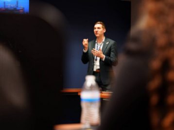 Detroit Tigers employee framed by two students speaking and gesticulating